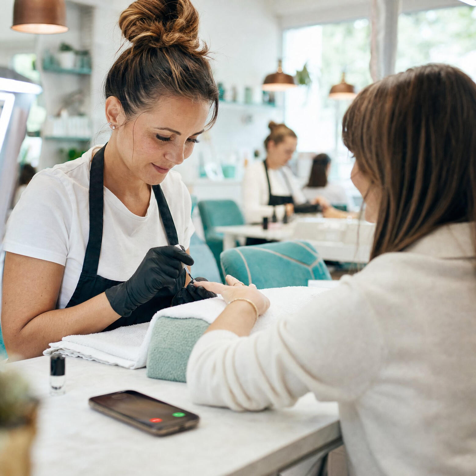 Nail technician giving a manicure while a phone lights up with an incoming call
